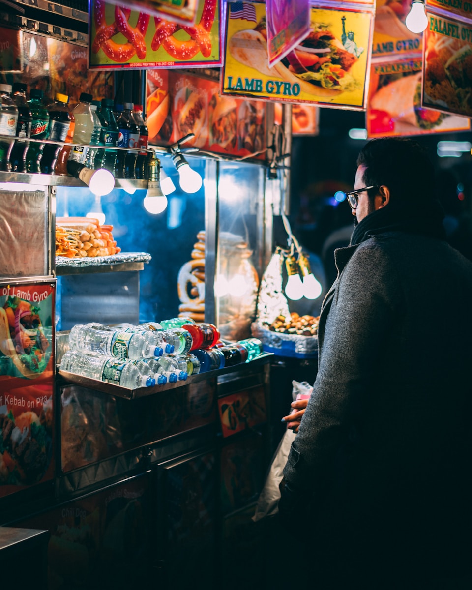 man with coat standing in front of food cart during nighttime