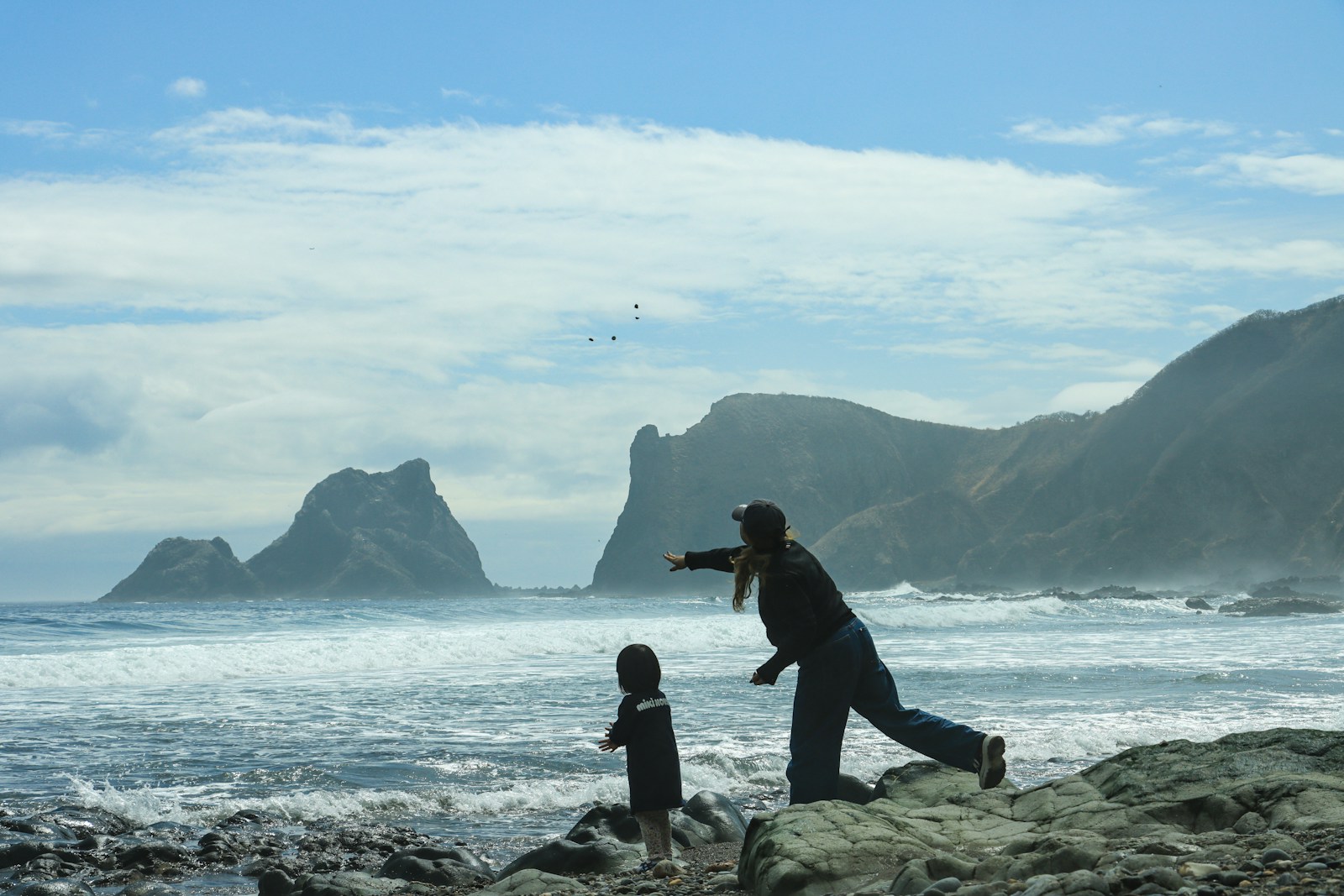 Woman and child on rocky coast with ocean waves
