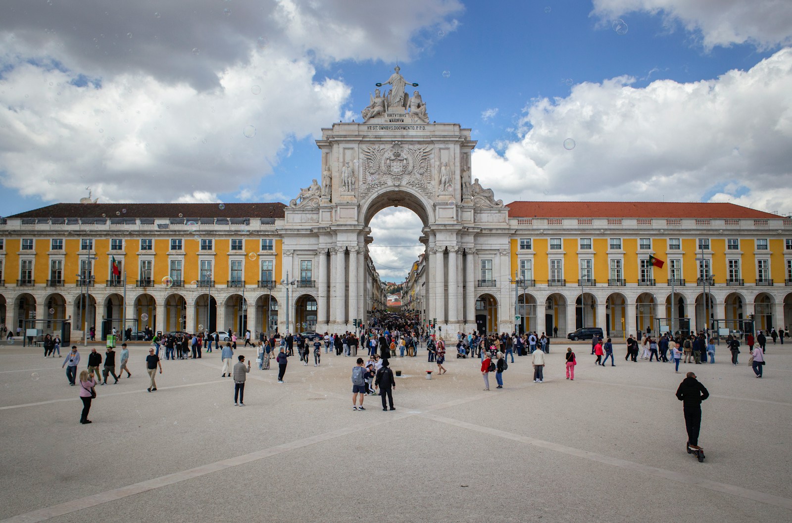 People gather in a grand european square with archway.