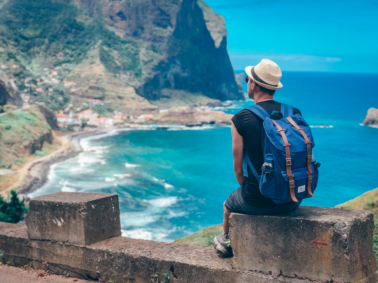 Man with backpack overlooks coastal village and ocean.